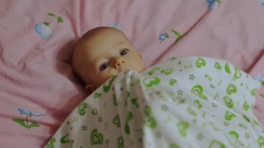 Küçük bir çocuk sırtüstü yatar, çarşafla oynar ve gülümser.. 