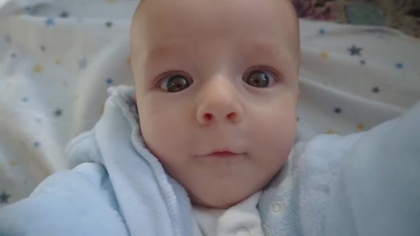 Divertido bebé se encuentra en la cama y mira a la cámara. — Vídeo de stock