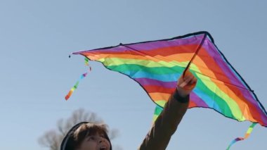 Mutlu bir çocuk uçan bir gökkuşağı uçurtmasıyla oynuyor.. 