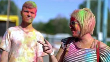 Holi renk festivali sırasında mutlu gençler dans edip kutlama yapıyor. Arka planda bir grup insan var.