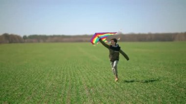 Bir çocuk elinde uçurtmayla yeşil bir arazide koşuyor. Ön manzara, yavaş çekim. Yüksek kaliteli FullHD görüntüler