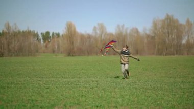 Bir çocuk elinde uçurtmayla yeşil bir arazide koşuyor. Ön manzara, yavaş çekim. Yüksek kaliteli FullHD görüntüler