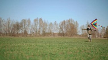 Bir çocuk elinde uçurtmayla yeşil bir arazide koşuyor. Yan görüntü, yavaş çekim. Yüksek kaliteli FullHD görüntüler