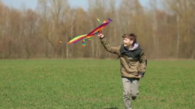 Bir çocuk elinde uçurtmayla yeşil bir arazide koşuyor. Ön manzara, yavaş çekim. Yüksek kaliteli FullHD görüntüler