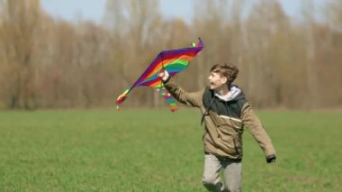 Bir çocuk elinde uçurtmayla yeşil bir arazide koşuyor. Ön manzara, yavaş çekim. Yüksek kaliteli FullHD görüntüler