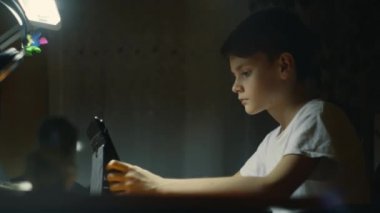 Genç bir çocuk akşamları masa başında ders çalışıyor. Çocuk deftere yazı yazıyor. Genç erkek çocuk odasında masasında ev ödevini yapmaya çok konsantre. Çocuklar ve eğitim. Yüksek kalite 4k görüntü