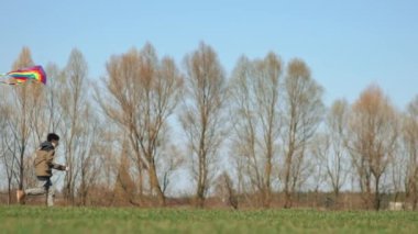 Bir çocuk elinde uçurtmayla yeşil bir arazide koşuyor. Yan görüntü, yavaş çekim. Yüksek kaliteli FullHD görüntüler