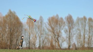 Bir çocuk elinde uçurtmayla yeşil bir arazide koşuyor. Yan görüntü, yavaş çekim. Yüksek kaliteli FullHD görüntüler