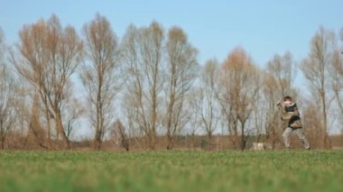 Bir çocuk elinde uçurtmayla yeşil bir arazide koşuyor. Yan görüntü, yavaş çekim. Yüksek kaliteli FullHD görüntüler