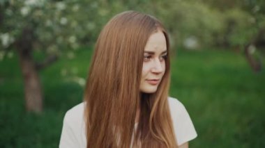 Parkta dururken gülümseyen ve kameraya bakan genç kız. Gülümseyen kızın sokak portresi. Parkta gülen neşeli kız.