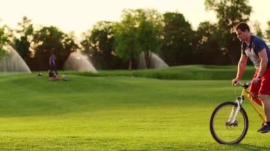 Bisikletçi gün batımında çimlerde geziyor. Yavaş giden bir bisikletçinin silüeti. Yüksek kalite 4k görüntü yavaş çekim.
