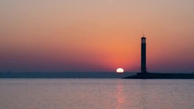 Uçsuz bucaksız bir göl ya da deniz üzerinde, deniz feneriyle kızıl bir güneşin doğuşu. Yüksek kalite 4k görüntü