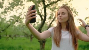 Çekici sarışın kadın gülümsüyor, akıllı telefonuyla selfie çekiyor, poz veriyor, saçını düzeltiyor. Alet kullanma kavramı.
