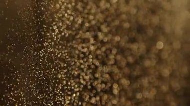 Yavaş çekimde siyah bir arkaplanda yüzen toz parçacıklarının güzel parıltısı. Bokeh etkisi. Çözülmüş altın parçacıkların arka planı. Soyutlama. Havada yüzen gerçek toz parçacıkları.