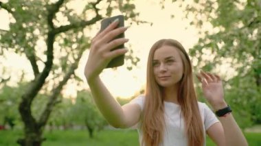 Çekici sarışın kadın gülümsüyor, akıllı telefonuyla selfie çekiyor, poz veriyor, saçını düzeltiyor. Alet kullanma kavramı.
