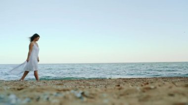 Çekici bir kız sahilde yürüyor ve güzel manzaraya hayran. Kız bir deniz manzarasına karşı sahile gidiyor.