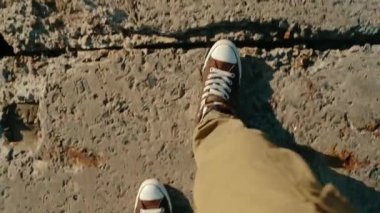 Legs in pants and sneakers walk on the concrete pavement. Walk. Top close-up view of the legs of a man walking on a concrete path. POV video