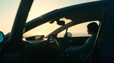 A young tourist girl gets out of the car to watch the sunset on the seashore. Trip, trip to nature. Leisure. Travel by car.