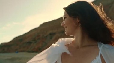 A girl standing on the seashore smiles covered with a white pareo and enjoys the sea breeze. Side view. Marine vacation