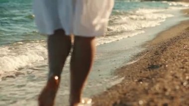 Girl walking barefoot along the sea coast. Close-up of a womans legs walking on the sea waves on a sandy beach. Back view. Tourism. Relaxation.