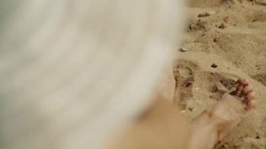 Pair of feet playing sand on the beach by the sea. Top view through the girls hat. Sunburn. Rest. Sunbathing.