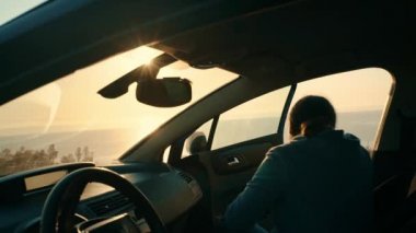 A young tourist girl gets out of the car to watch the sunset on the seashore. Trip, trip to nature. Leisure. Travel by car.