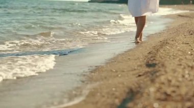 Close-up of womans legs walking on a sandy beach with waves. Front view