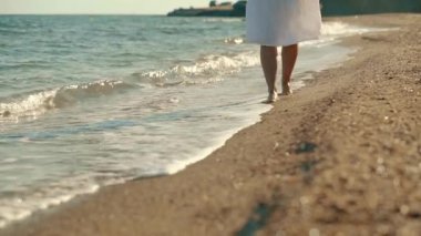 Close-up of womans legs walking on a sandy beach with waves. Front view
