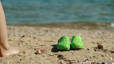 Flip flops, a hat and sunglasses close-up on the sand against the backdrop of a girl walking towards the sea.