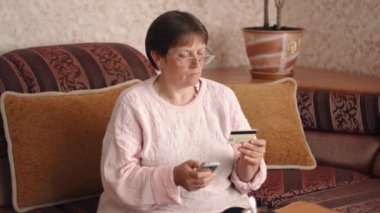 Portrait of a woman in glasses who makes purchases online using a credit card and a smartphone. Using a credit card online. Online shopping or making payments. High quality 4k footage