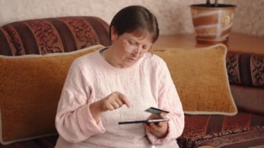 Portrait of a woman in glasses who makes purchases online using a credit card and a tablet. Using a credit card online. Online shopping or making payments. High quality 4k footage