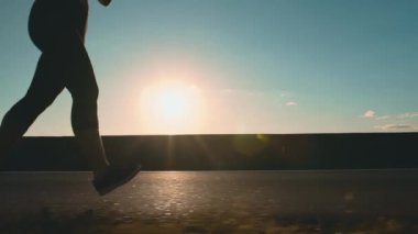 Woman running on the road at sunset. Silhouette of running female legs. Girl jogging, side view. Running endurance training.High quality 4k footage