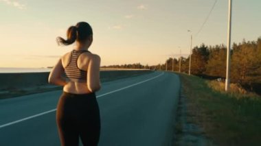 A young girl is engaged in sports jogging on the road against the background of the sky and grass. Healthy, active lifestyle.View from the back.High quality 4k footage