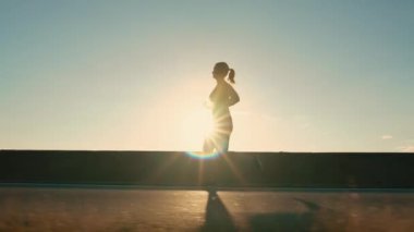 Silhouette of a girl jogging along the road in the rays of the setting sun, side view. High quality 4k footage