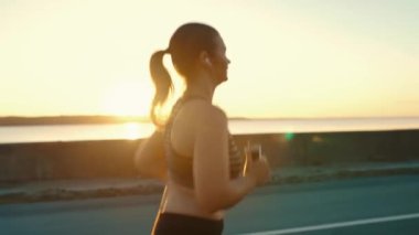  A girl in headphones, listening to music, runs along the road against the background of the embankment. Healthy, active lifestyle. View from the back.High-quality shooting in 4k format.
