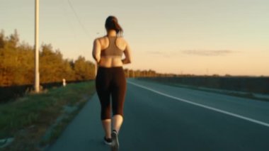 A young girl is engaged in sports jogging on the road against the background of the sky and grass. Healthy, active lifestyle.View from the back.High quality 4k footage