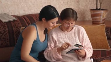 Portrait of a middle-aged woman with glasses and a girl who helps to shop online using a credit card and a tablet. Using a credit card online Online shopping or making payments. 4k