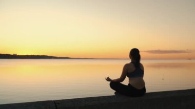 Silhouette of a girl meditating by the lake at sunset. Feeling of calmness and peace. Side view. High quality 4k footage