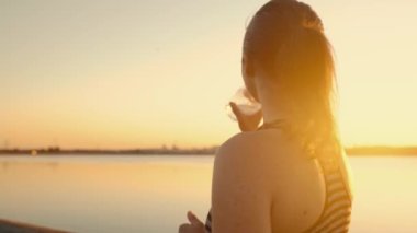 The athlete replenishes the water balance after running on the embankment in the rays of sunset.Portrait of an athlete girl drinking water from a bottle at sunset by the lake.High quality 4k footage