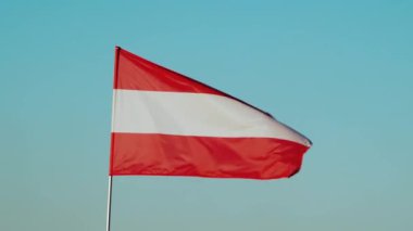 Avusturya 'nın ulusal bayrağı açık mavi gökyüzüne karşı rüzgarda hafifçe dalgalanıyor. Döngülü animasyon. Ülkenin ulusal kimliği. Yüksek kalite 4K görüntü.