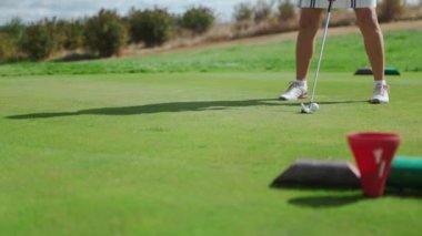 Golf sahasında golf arabasının arkasından bir golfçünün görüntüsü. Kendine güvenen sporcu kadın ısınıyor ve golf sopasıyla topa vuruyor. Açık hava eğlencesi ve spor konsepti.