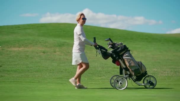 Kvinna Vit Kostym Går Längs Golfbanan Och Bär Klubbor Golfvagn — Stockvideo