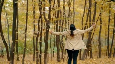 Kız sonbahar parkında, düşen renkli yaprakların altında döner ve güler. Güzel genç kadın sonbahar parkında eğleniyor. Sarı yapraklar. Doğanın güzelliği.