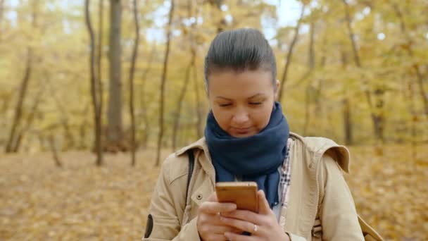 Een Jong Meisje Staat Een Herfstpark Met Een Mobiele Telefoon — Stockvideo