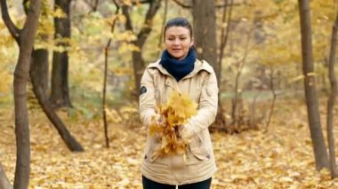 Neşeli kız düşen sonbahar yapraklarını toplar ve fırlatır. Düşen yaprakları izler ve eğlenir. Neşeli anlar. Sonbahar parkında yürüyor. Yüksek kalite 4k görüntü