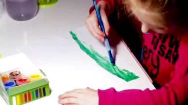 Çocuk bir fırçayla beyaz bir manzara örtüsüne gouache boyalarıyla resim çiziyor. Çocukların yaratıcılığı. Boyalarla çizim yapmak. Sanat terapisi.