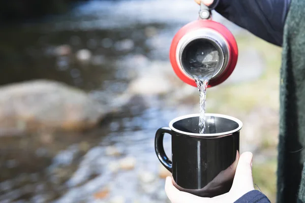Young woman pouring hot water in a mug. Beside a river. Latin beverage. — Stockfoto