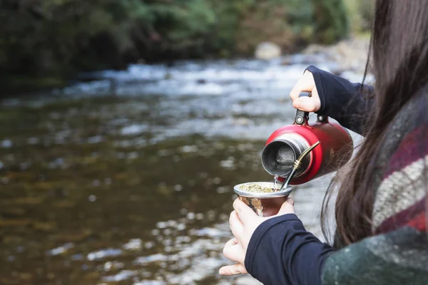 Young woman serving mate in a natural space. Beside a river. Latin beverage. — Stockfoto