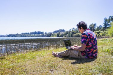 Genç latin adam gölden uzaktan kumandayla iş yapıyor. Telesekreter konsepti. Dijital Göçebe