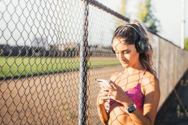 Genç aktif bir kadın, spor yapmadan önce siyah kablosuz kulaklık kullanıyor ve akıllı telefonuna müzik listesi koyuyor..